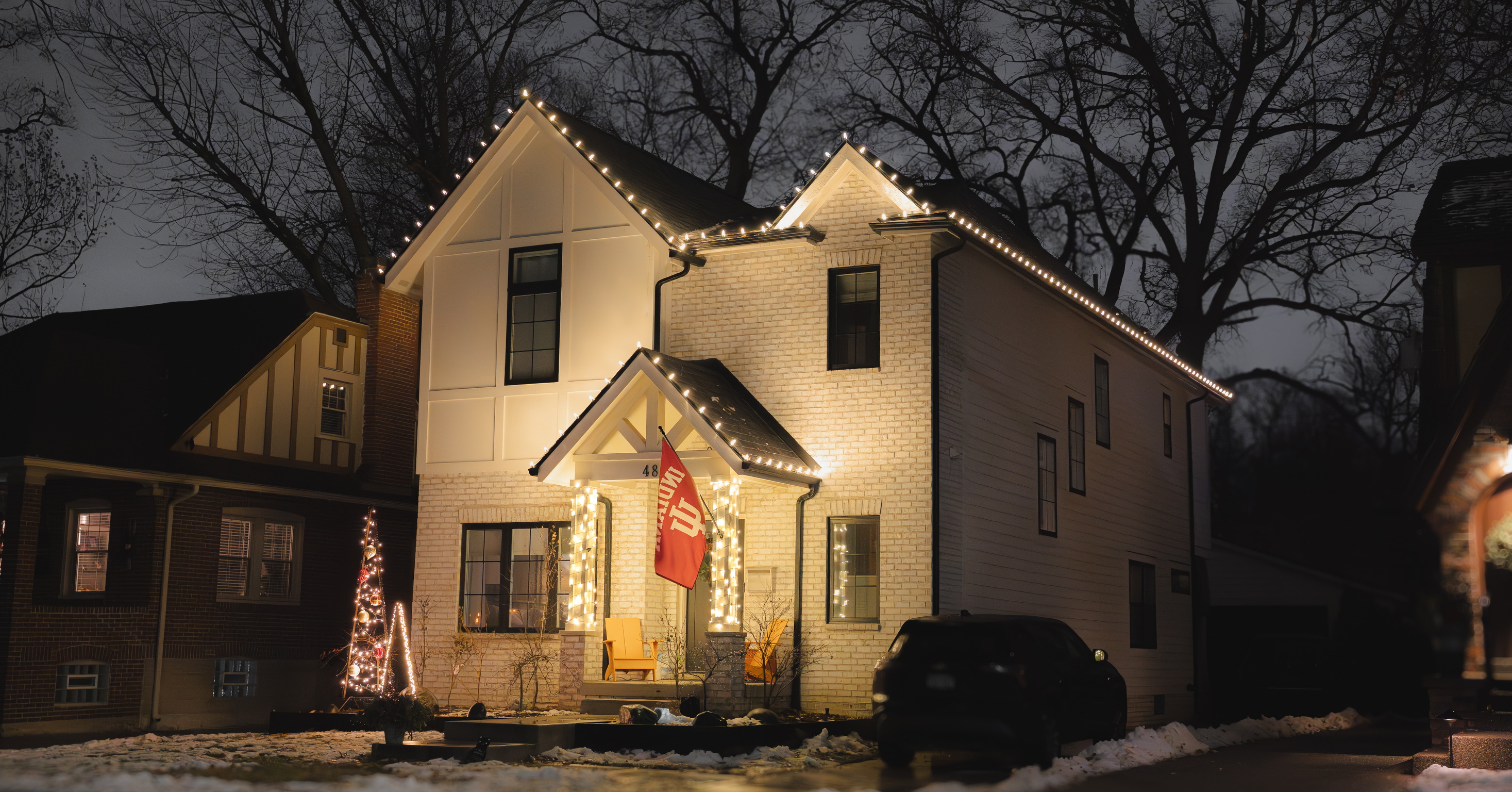 White brick home outlined in warm white holiday lights with illuminated porch columns